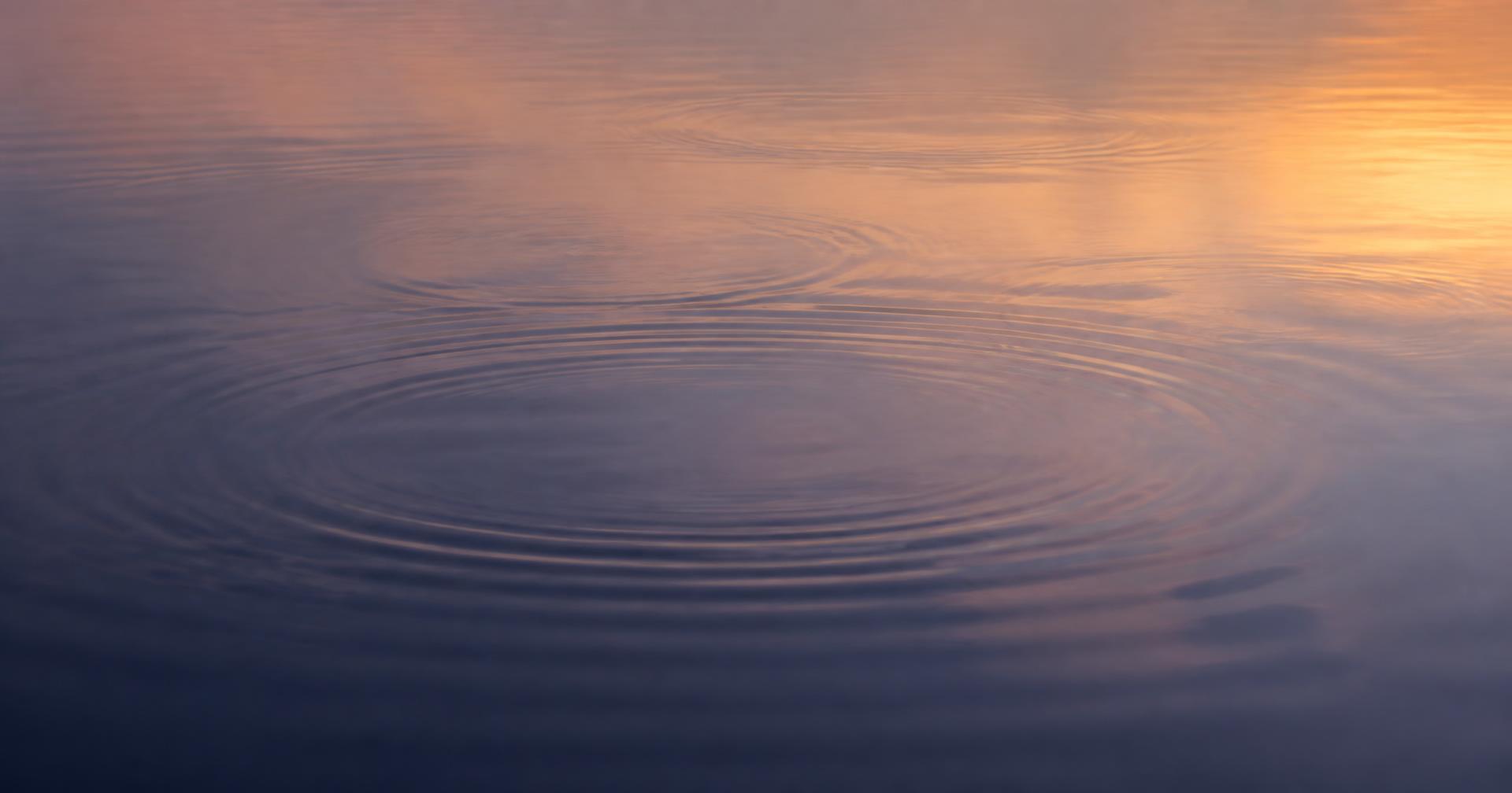 Soft ripples spreading across still water at dusk
